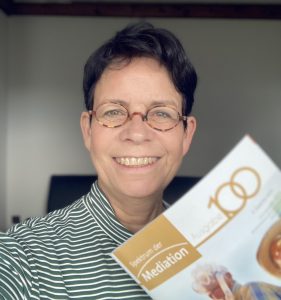 Das Bild zeigt Marja Költzsch im Frontprofil. Vor sich hält sie das Magazin "Spektum der Mediation", für das sie einen Artikel geschrieben hat zum Thema "Mediation bei Erkrankung in Familien."